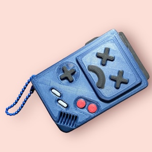 May include: A blue 3D printed keychain shaped like a retro handheld game console with black buttons and a red button. The keychain has a silver chain.