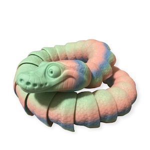 Op de afbeelding: Een kleurrijk, gesegmenteerd slangen speelgoed gemaakt van zacht, getextureerd plastic. De slang is opgerold in een cirkel en heeft een lichtgroene kop met roze en blauwe accenten.