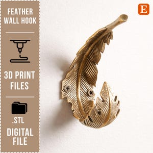 Könnte beinhalten: Ein goldfarbener Feder-Wandhaken an einer weißen Wand. Der Haken ist aus Metall gefertigt und hat ein detailliertes Federdesign. Der Text auf der linken Seite lautet "FEATHER WALL HOOK", "3D PRINT FILES" und ".STL DIGITAL FILE".