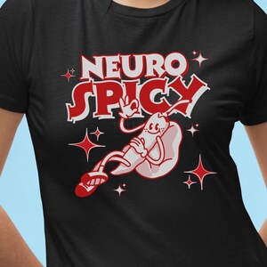Może przedstawiać: Czarna koszulka z napisem "NEURO SPICY" w kolorze czerwono-białym, z postacią z kreskówki przedstawiającą papryczkę chili. Koszulka ma również czerwone gwiazdki i logo Wildaza T-Shirt Co.
