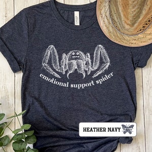 May include: A dark heather navy blue t-shirt with a white illustration of a spider and the text "emotional support spider".