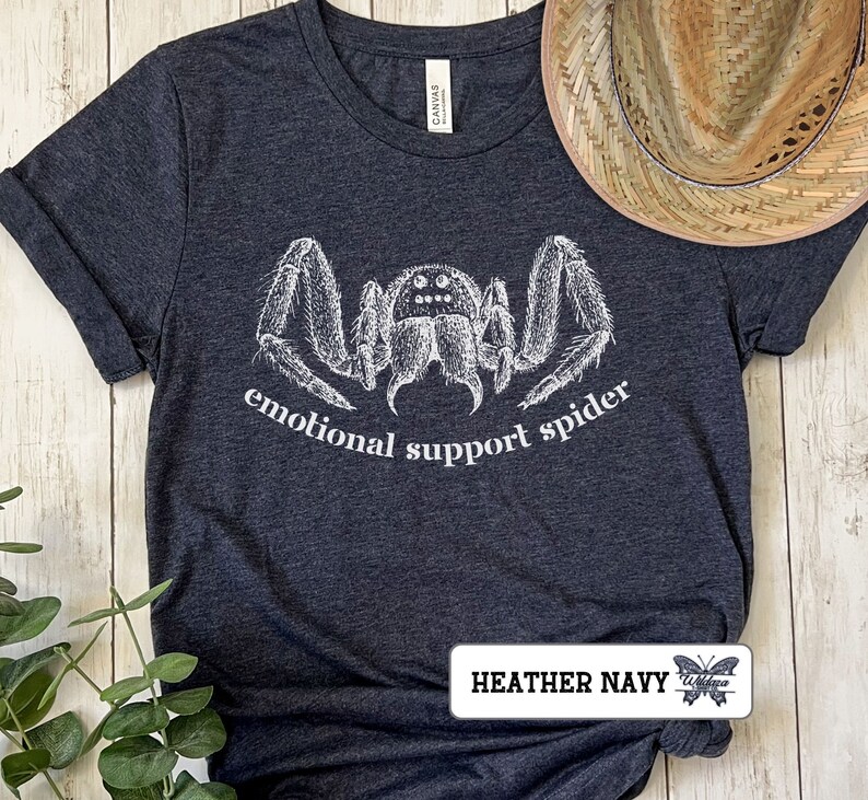 May include: A dark heather navy blue t-shirt with a white illustration of a spider and the text "emotional support spider".