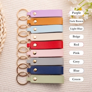 May include: A collection of leather keychains in various colors, including purple, brown, light blue, beige, red, pink, grey, blue, and green. Each keychain has a gold-colored ring and a snap closure.
