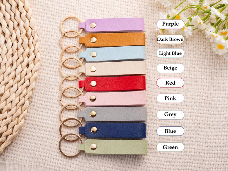 May include: A collection of leather keychains in various colors, including purple, brown, light blue, beige, red, pink, grey, blue, and green. Each keychain has a gold-colored ring and a snap closure.