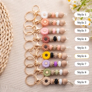 May include: A collection of nine keychains with gold-colored hardware. Each keychain features a variety of colorful silicone beads, wooden beads, and decorative flower accents. The text "Style 1" through "Style 9" is visible.