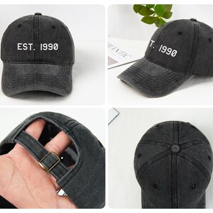 May include: A dark gray baseball cap with the text "EST. 1990" in white. The cap has a curved brim and an adjustable strap with a metal buckle. The hat is made of a worn, faded material.