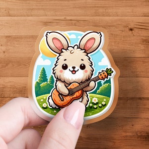May include: A sticker featuring a cartoon bunny playing a carrot-shaped guitar. The bunny has fluffy beige fur, pink ears, and is set against a backdrop of a sunny meadow with trees and flowers. The sticker has a brown border.