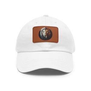 May include: White baseball cap with a curved brim. The cap features a rectangular patch with a lion's face split in half, one side white and the other brown. The patch is on a brown background.