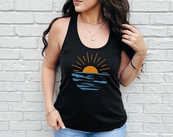 May include: Black racerback tank top featuring a sunset graphic. The design includes an orange sun with yellow rays over blue water. The tank top is made of a soft, comfortable material.