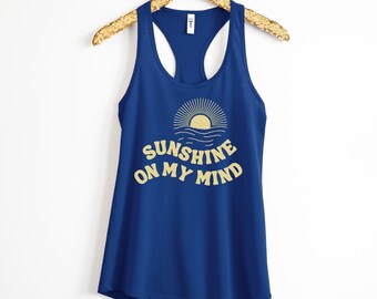 May include: A royal blue tank top with a yellow graphic of a sun setting over the ocean and the text "Sunshine on my mind".