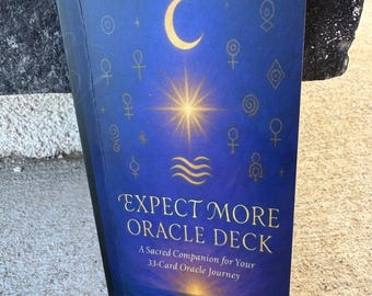 May include: A blue oracle deck titled "EXPECT MORE ORACLE DECK" with gold lettering and celestial illustrations. The cover features a crescent moon, a starburst, and other symbols. The author's name, DR. BURNETTA THOMAS, is at the bottom.