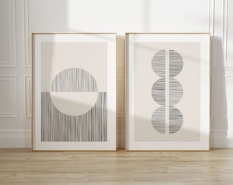 Puede incluir: Dos impresiones artísticas abstractas enmarcadas. Una presenta un semicírculo y un semicírculo con líneas verticales. La otra tiene tres círculos apilados con líneas horizontales. Ambas tienen marcos dorados y fondos neutros.
