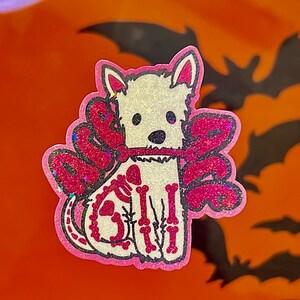 May include: A white dog wearing a pink sparkly costume with the word "Boo" on it. The dog is wearing a skeleton costume with pink bones and a pink heart on its chest.
