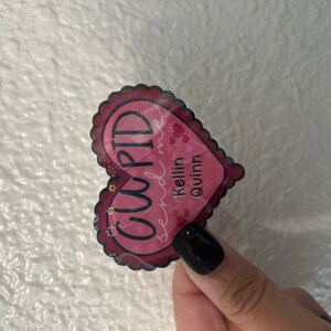 May include: Pink heart-shaped sticker with the text "CUPID send me Kellin quinn" in black lettering.