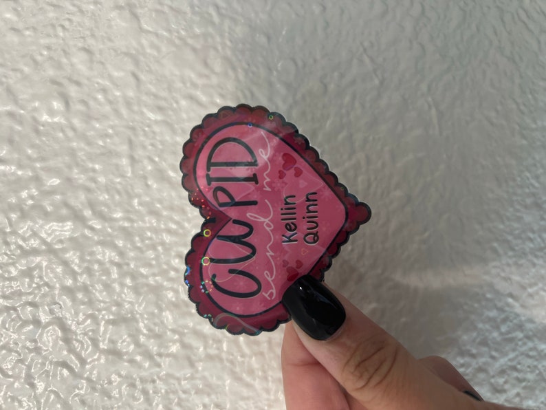 May include: Pink heart-shaped sticker with the text "CUPID send me Kellin quinn" in black lettering.