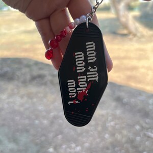 K&ouml;nnte beinhalten: Schwarzer Motel-Schl&uuml;sselanh&auml;nger mit roten und wei&szlig;en Perlen. Der Schl&uuml;sselanh&auml;nger tr&auml;gt den Text "I love you" mit einem roten Blutfleck.