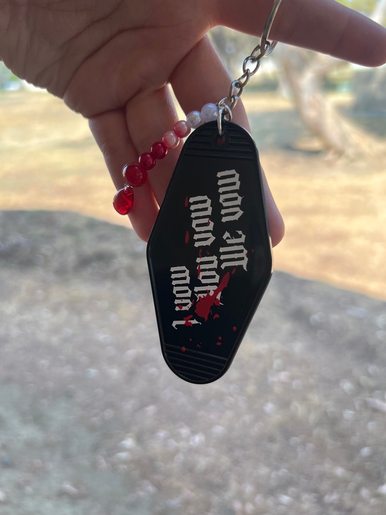 K&ouml;nnte beinhalten: Schwarzer Motel-Schl&uuml;sselanh&auml;nger mit roten und wei&szlig;en Perlen. Der Schl&uuml;sselanh&auml;nger tr&auml;gt den Text "I love you" mit einem roten Blutfleck.