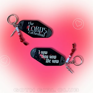 Puede incluir: Dos llaveros negros con cuentas rojas y blancas. Un llavero tiene el texto "the LORDS cathedral" y el otro llavero tiene el texto "I vow you vow we vow".