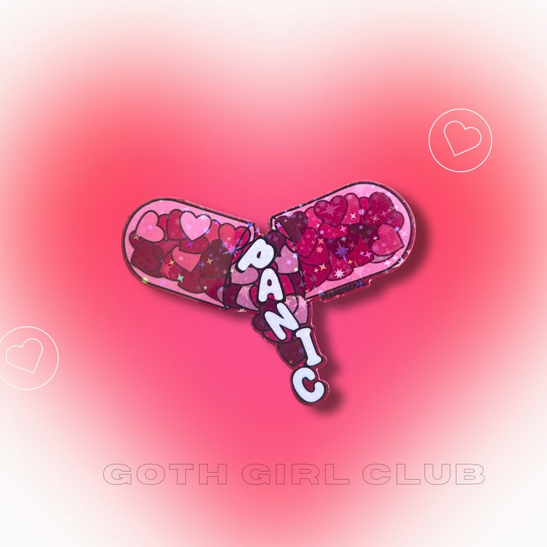 May include: A pink and red pill-shaped pin with the word "PANIC" written in white letters. The pill is broken open and filled with pink and red glitter hearts.