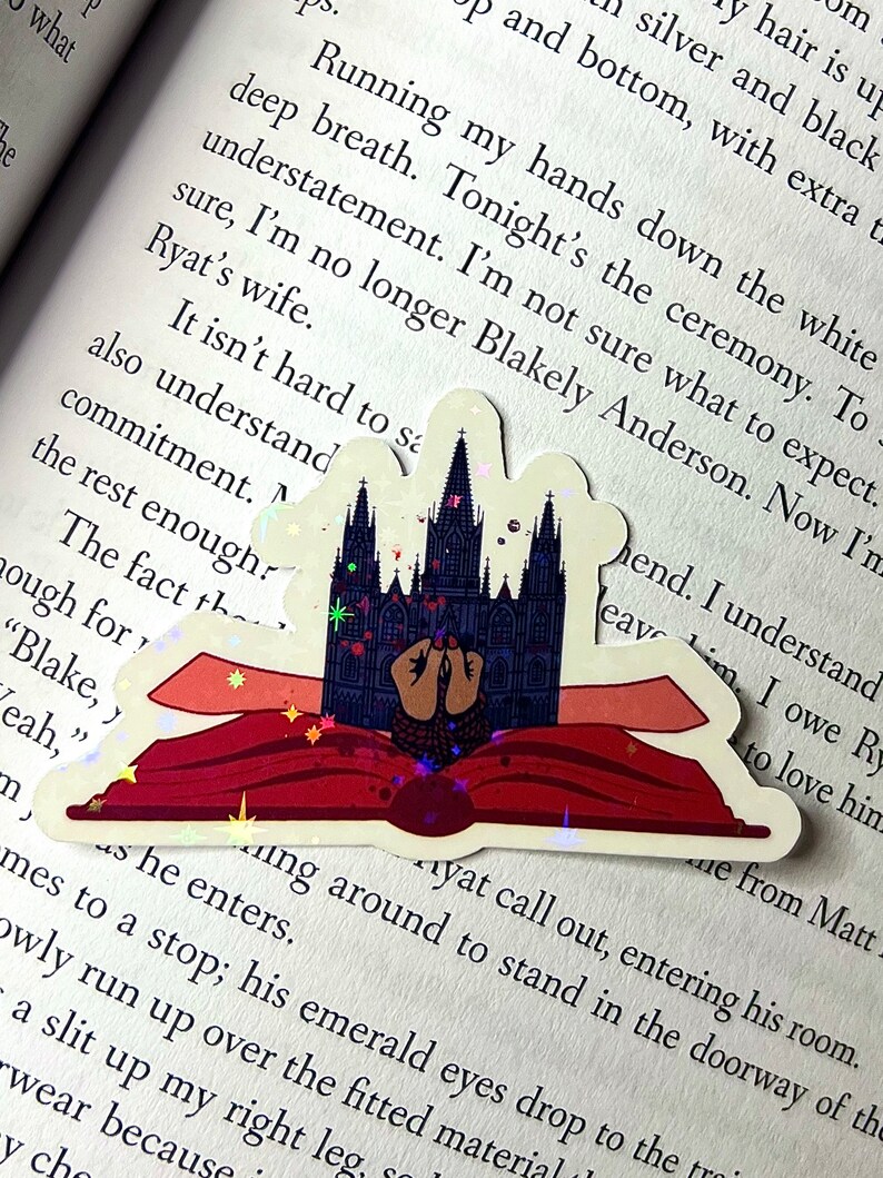 May include: A sticker of a book with a gothic cathedral on the cover. The book is open and the cathedral is glowing with a magical effect. The sticker is on a page of a book with text that reads "Running my hands down the white deep breath. Tonight's the ceremony. To sure, I'm no longer Blakely Anderson. Now I'm Ryat's wife. It isn't hard to sa also understand commitment. The fact th ough for "Blake, y Yeah," m  Ayat call out, entering his room.  as he enters. mes to a stop; his emerald eyes drop owly run up over the fitted materia a slit up my right leg. wear because. y cho"