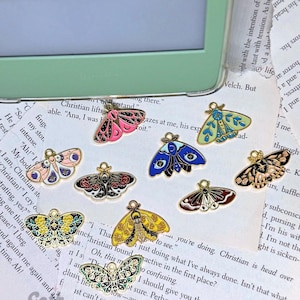 May include: A set of nine gold-toned metal charms featuring colorful butterfly designs. Each charm has a loop for attaching to a necklace, bracelet, or keychain. The butterflies are painted with various colors, including blue, green, red, black, and white.