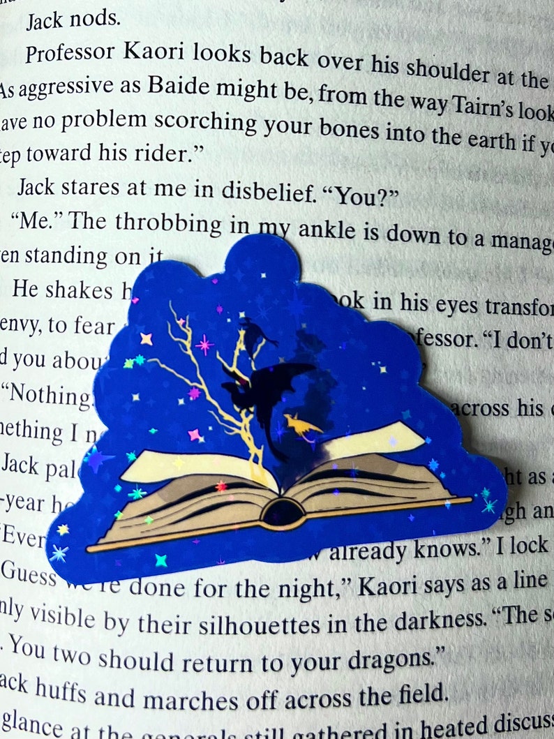 May include: A blue and silver glitter book bookmark with a black silhouette of a dragon and a tree with stars. The bookmark is on top of an open book with the text "already knows." "I lock" "Guess we're done for the night," Kaori says as a line only visible by their silhouettes in the darkness. "The s" "You two should return to your dragons."