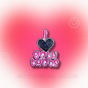 May include: Pink and black enamel pin with a heart and the text "I love goth thots". The pin has a white outline and a shadow effect. The text "GOTH GIRL CLUB" is printed below the pin.
