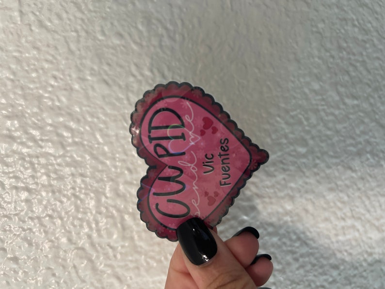 May include: A pink heart-shaped sticker with the word "CUPID" written in black and the text "send love" and "Vic Fuentes" written in white.