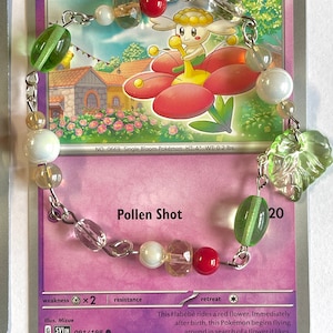May include: A Flabébé Pokémon trading card from the Sword & Shield set. The card features a light pink background with a green, white, and red flower. The card number is 091/198. The card text reads: "This Flabébé rides a red flower. Immediately after birth, this Pokémon begins flying around in search of a flower it likes."