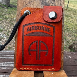 May include: A red leather wallet with a black strap and the words "AIRBORNE" and "AA" embossed on the front.