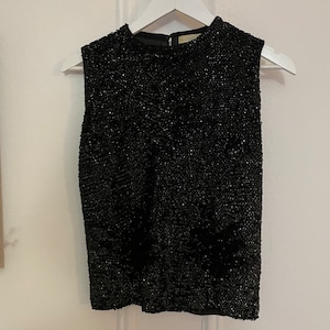 May include: A black sleeveless top with a sparkly texture. The top has a round neckline and a loose fit.