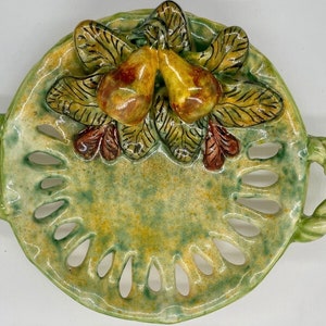 May include: A green ceramic dish with two pears and leaves in relief. The dish has two handles and a scalloped edge.