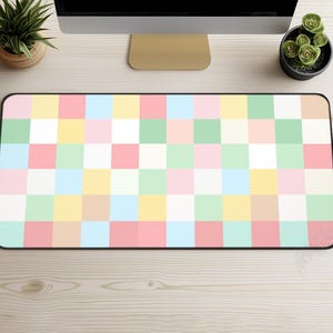 May include: A rectangular desk mat featuring a pastel checkered design in pink, green, yellow, blue, and white. The mat has a black border and is on a light wood-grain surface. The mat is designed to protect the desk surface.