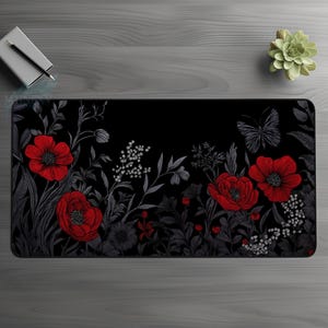 May include: A rectangular black desk mat featuring a floral design with red poppies and a butterfly. The flowers and foliage are set against a dark background, creating a striking contrast. The mat is designed for use with a computer.