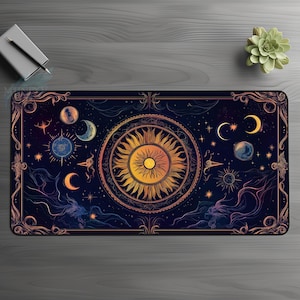 Puede incluir: Una alfombrilla de ratón negra y dorada con un diseño celestial que presenta un sol, una luna y estrellas. El sol está rodeado por un halo dorado y la luna tiene forma de media luna. Las estrellas están dispersas por el fondo.