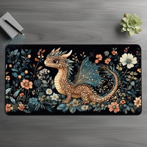 Può includere: Un tappetino per mouse nero con un'illustrazione colorata di un piccolo drago marrone con ali blu in un campo di fiori. Il drago ha un corpo marrone chiaro con accenti arancioni e un'ala blu chiaro con macchie bianche.