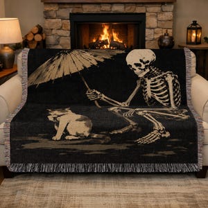 Può includere: Coperta nera con uno scheletro che tiene un ombrello e un gatto. Lo scheletro e il gatto sono beige su sfondo scuro. La coperta ha un bordo con frange. Ideale per un divano.