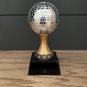 May include: A silver disco ball trophy with a gold base and black base. The base has a ring of gold stars around the top.