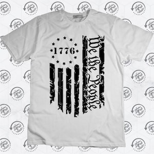 May include: White t-shirt featuring a black distressed American flag design. The flag has 13 stripes and 13 stars in a circle with the year "1776" in the centre. The words "We the People" are written vertically on the right side of the flag.