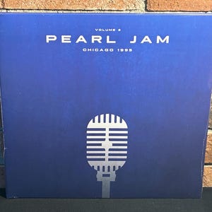 May include: A blue vinyl record album cover with the text "Pearl Jam" and "Volume 2 Chicago 1995" in white. A silver microphone icon is in the center of the cover.