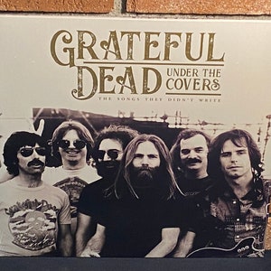 May include: A black and white photo of the Grateful Dead band members on a record album cover. The album title is "Grateful Dead Under the Covers: The Songs They Didn't Write".