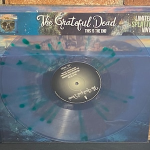 May include: A clear blue vinyl record with a green splatter design. The record is in a protective sleeve with the text "The Grateful Dead" and "This Is The End" printed on the front. The record is labeled "The Grateful Dead" and has a limited edition splatter vinyl label.
