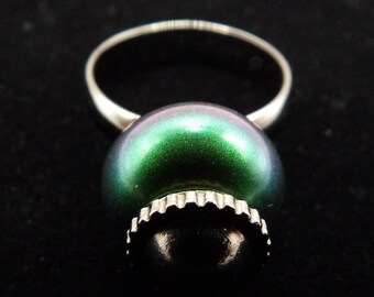 Puede incluir: Un anillo de plata con una gran perla verde y negra iridiscente.