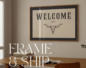 May include: A framed print with a black and white illustration of a longhorn skull with the text "WELCOME HOME" above it. The frame is brown wood with a black mat.