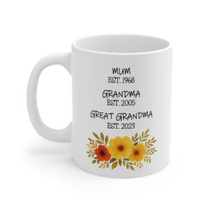 Op de afbeelding: Witte keramische mok met zwarte tekst die "Mum Est. 1968 Grandma Est. 2005 Great Grandma Est. 2023" luidt en een bloemmotief met gele en oranje bloemen.