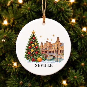 May include: A round white ceramic ornament featuring a colourful illustration of a decorated Christmas tree with red and gold baubles, a bright orange fruit, and the Plaza de España in Seville, Spain, with the text SEVILLE printed below.
