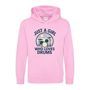 Puede incluir: Sudadera con capucha rosa claro con el texto azul marino "JUST A GIRL WHO LOVES DRUMS". El gráfico presenta una batería dentro de un círculo con una luna y estrellas. La sudadera tiene un bolsillo delantero y una capucha con cordón.