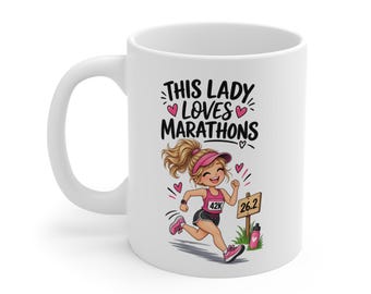 May include: A white ceramic mug featuring a cartoon illustration of a runner with blonde hair in a ponytail, wearing a pink visor and tank top. The text reads THIS LADY LOVES MARATHONS above the runner, with a sign marked 26.2 and a water bottle.