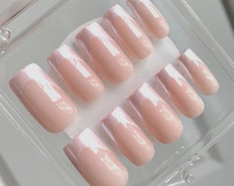 May include: A set of artificial nails in a clear plastic case. The nails are a light pink with a white tip, and are arranged in two rows. The nails have a glossy finish.