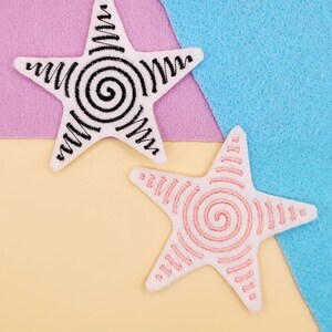 May include: Two white star-shaped patches with embroidered spiral designs. One star features a black spiral, the other a pink spiral. The patches are on a colorful background of pink, blue, and yellow.